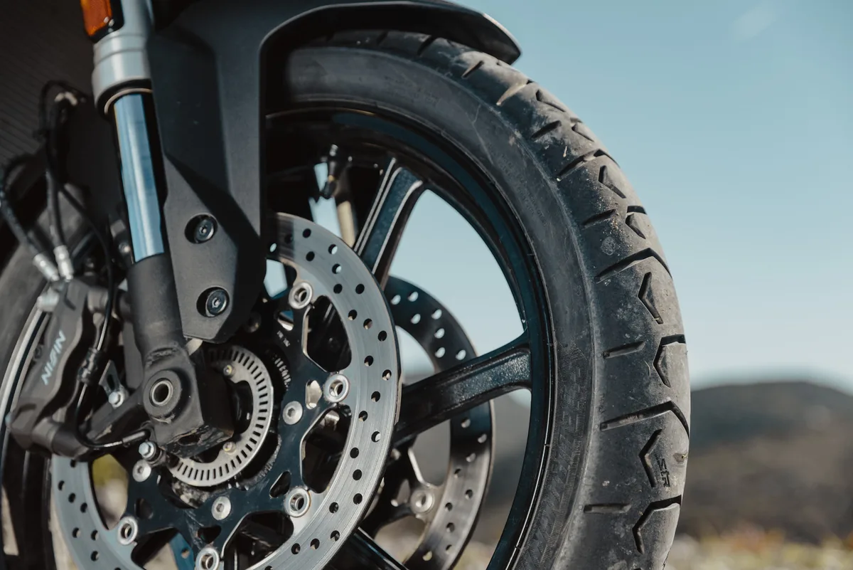 Close-up of the front wheel, fork and brake disc with the tyre sidewall.