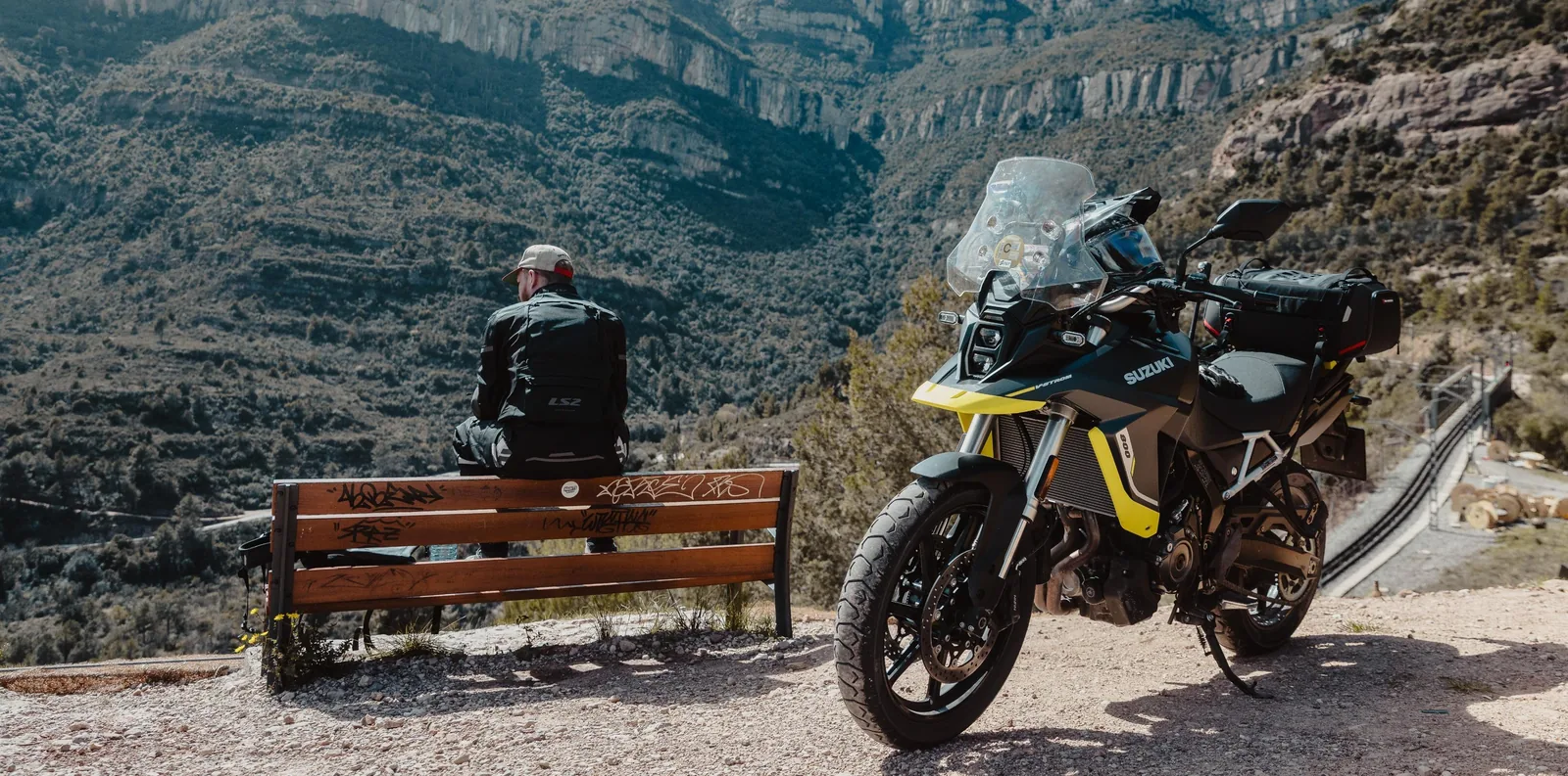Kanyona bakan bir seyir terasinda park etmis adventure motosiklet; surucu bankta oturuyor.
