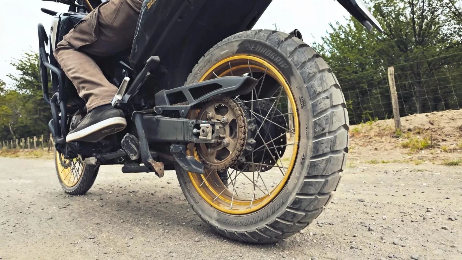 Agaclarla cevrili cakil yolda ilerleyen adventure motosiklet.