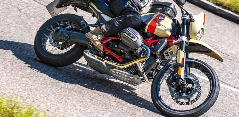 Kirlik bir virajda yatmis, yukleri takili adventure motosiklet.
